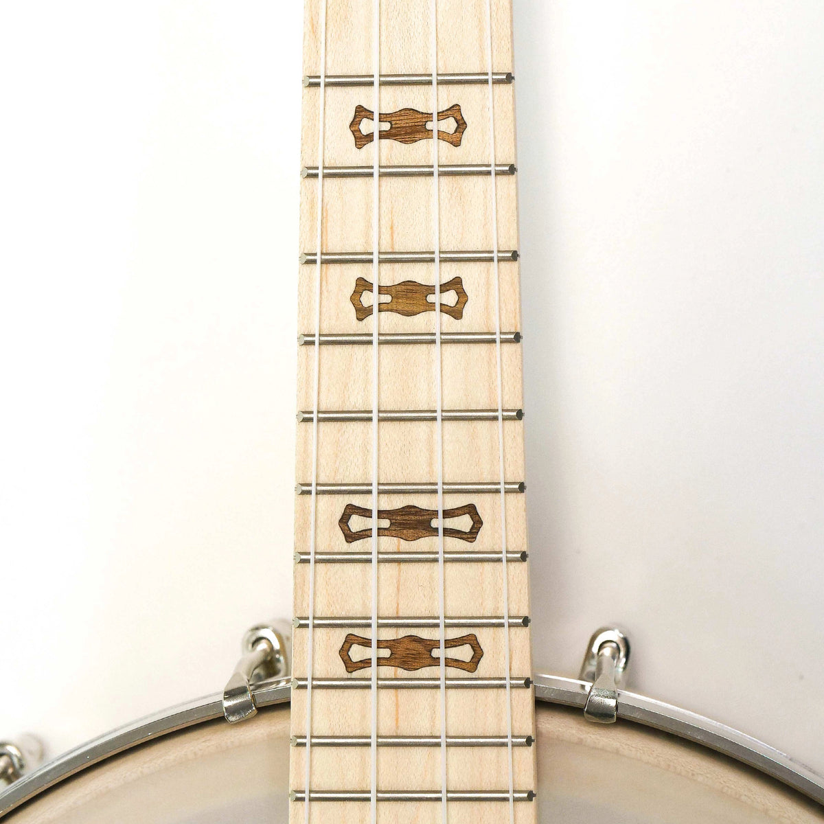 Close-up of a light natural wood banjo neck with metal strings and decorative inlays, photographed against a plain white background with part of a drum rim visible at the bottom.