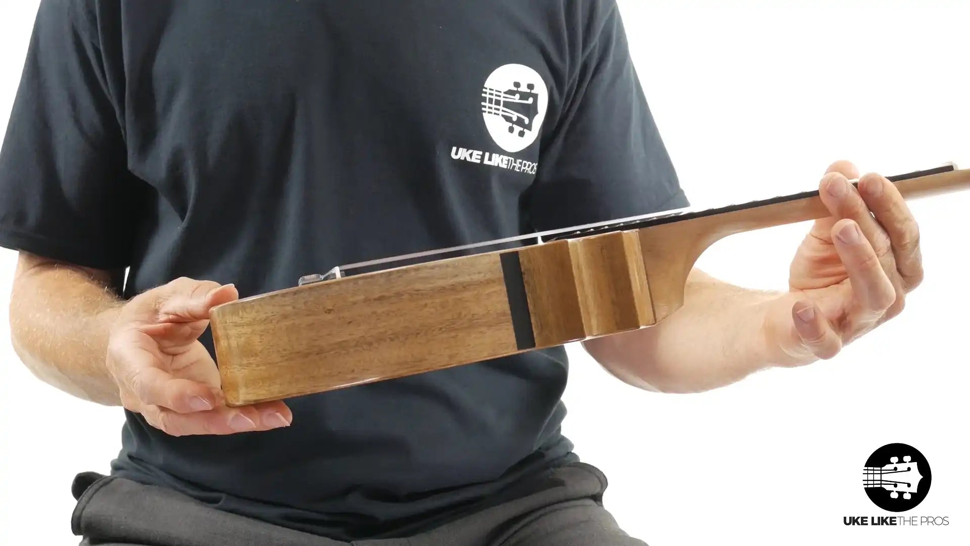 Side view of natural wood ukulele body, held by person in black shirt at Terry Carter Music Store.