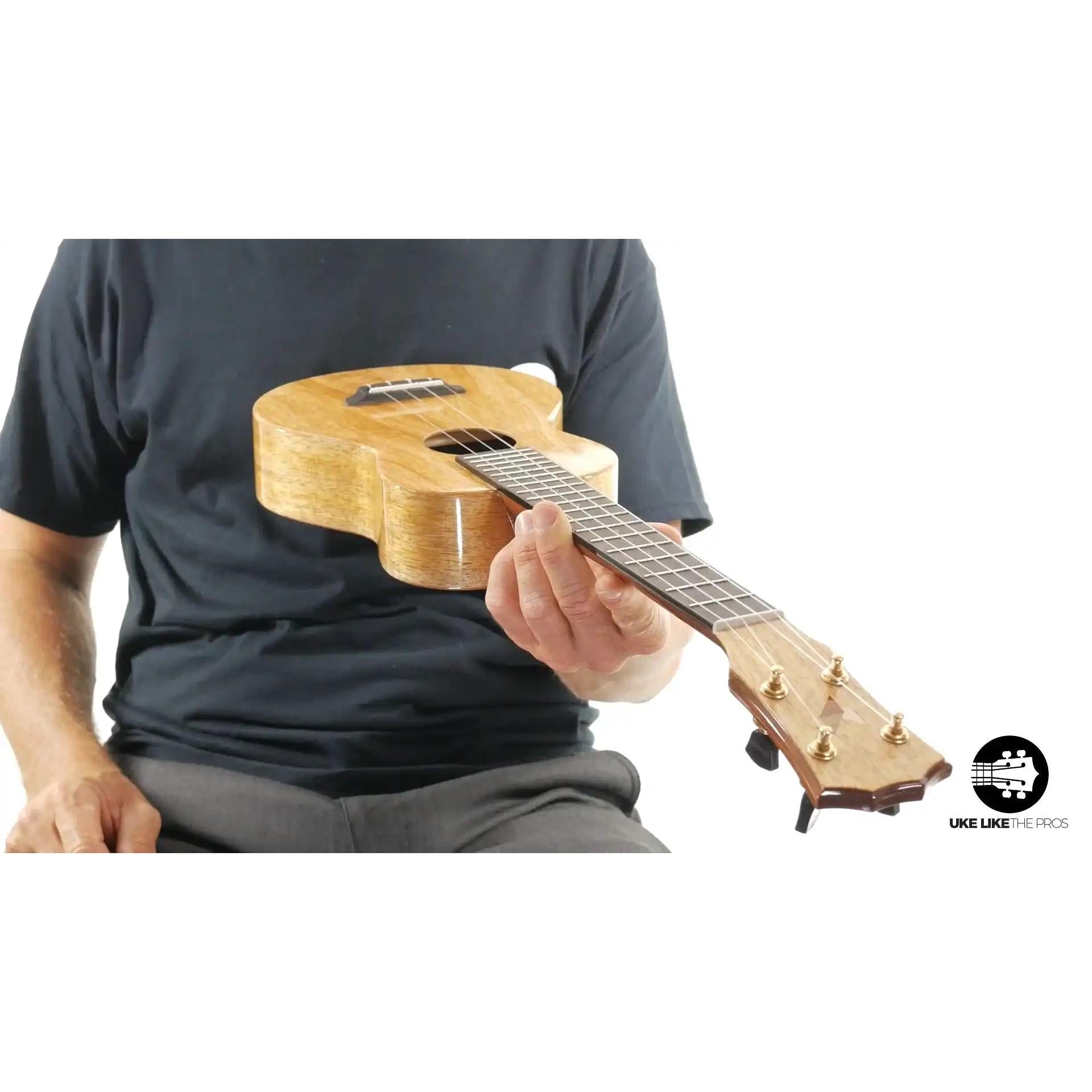 Natural wood ukulele with gold tuners, held by seated person, available at Terry Carter Music Store.