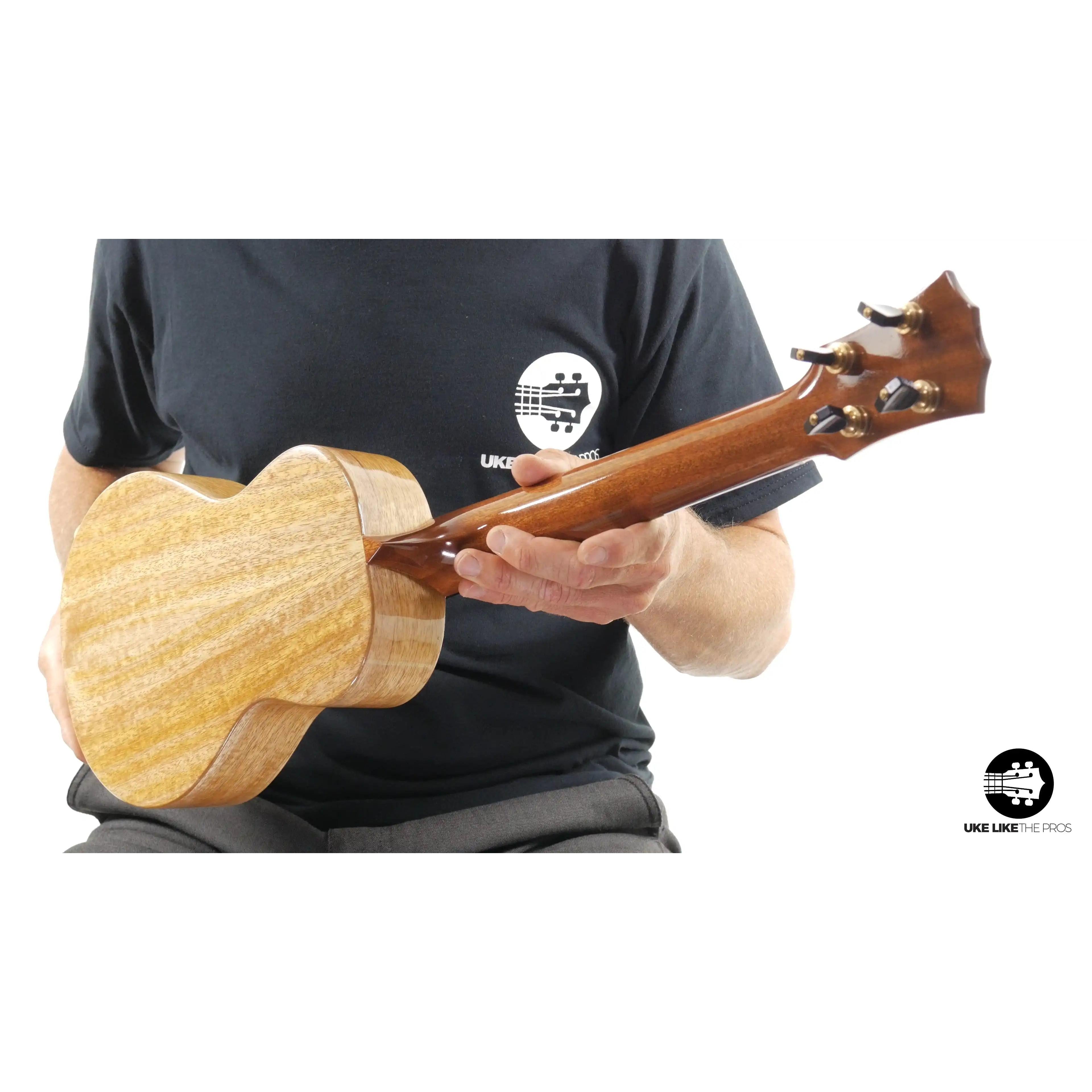 Back of natural wood ukulele headstock and body, held by person, Terry Carter Music Store