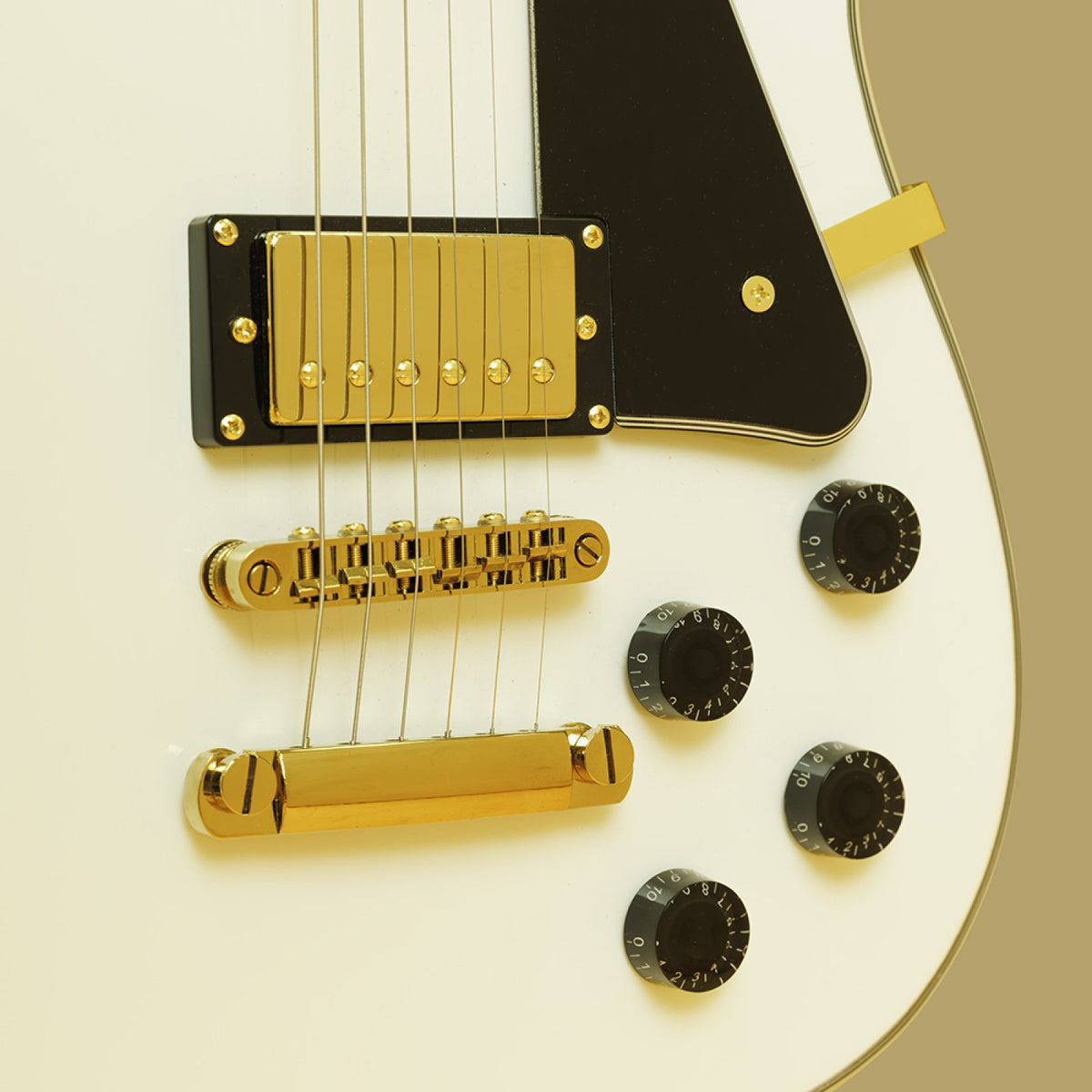 Close-up of the gold-cover humbucker, tune-o-matic bridge, tailpiece and control knobs on the white Stagg 30th Anniversary Legacy guitar