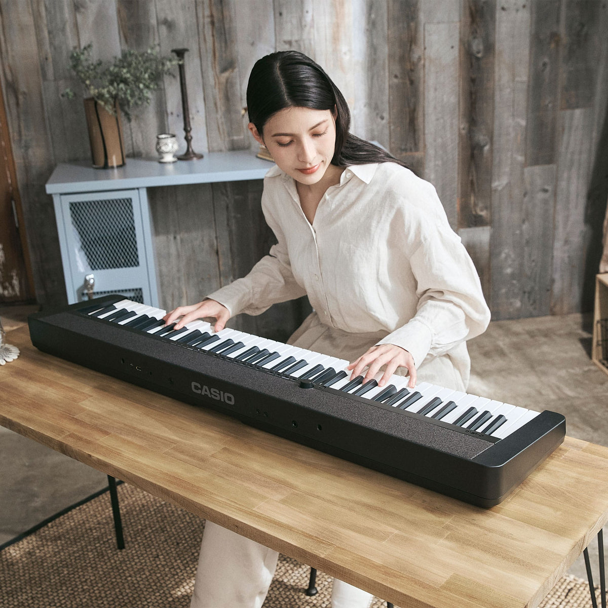 Person playing a black Casio CT-S1-76BK keyboard at a wooden table, with the CASIO logo on the rear panel