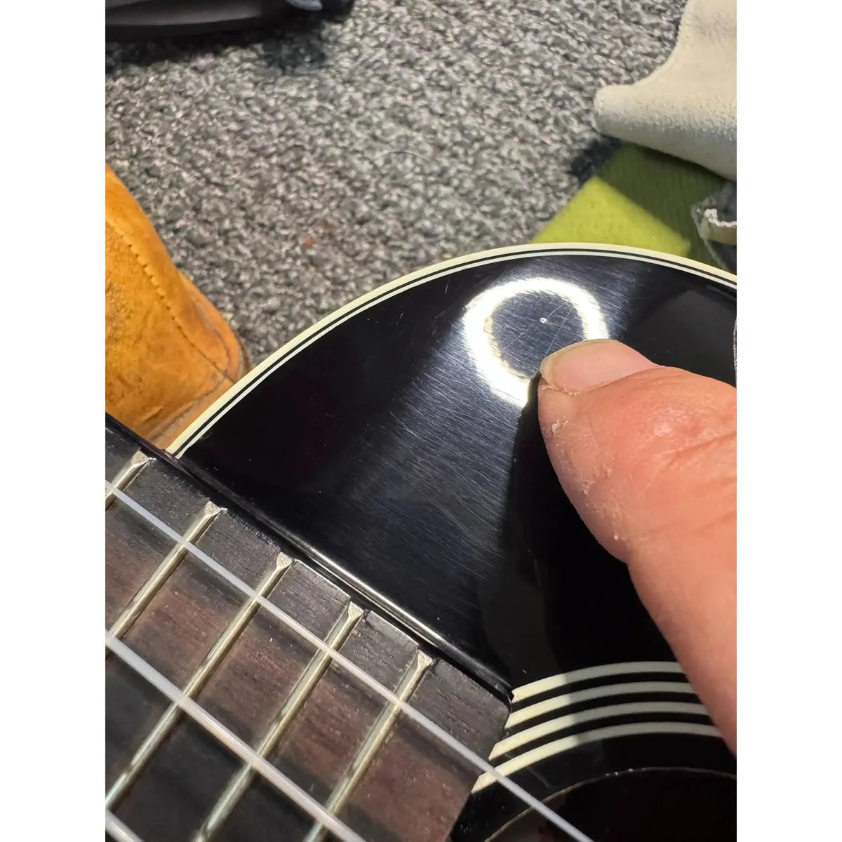 Close-up of a finger pointing to a small nick and surface swirls on the gloss sunburst Kala tenor ukulele body.
