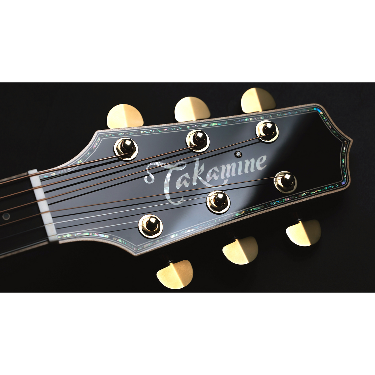Black headstock of Takamine THE 60TH with the Takamine logo, abalone edging and gold tuners.