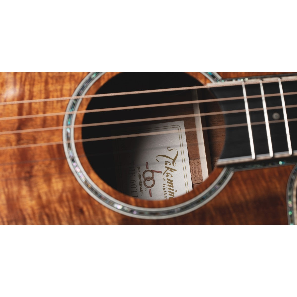 Close-up inside the soundhole of Takamine THE 60TH showing the numbered 60th anniversary label, abalone rosette and figured Hawaiian koa top.