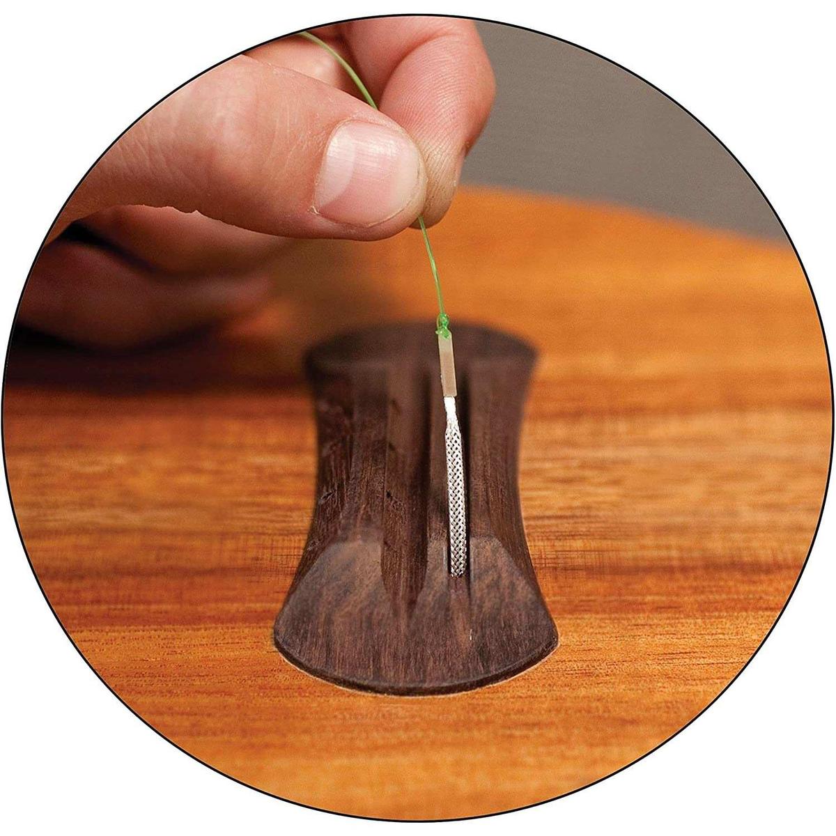 Hand installing guitar string on wooden bridge, close-up at Terry Carter Music Store